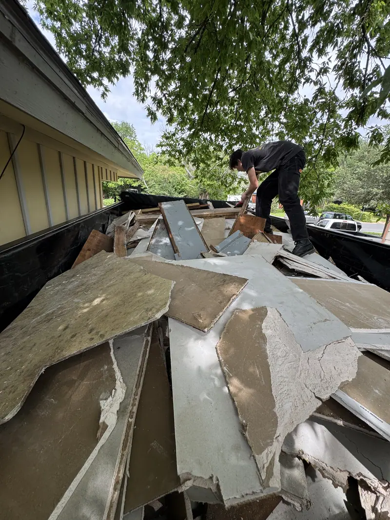 Elite Demo and Junk Removal crew member standing in the dump trailer stacking torn out siding and debris at an Austin house