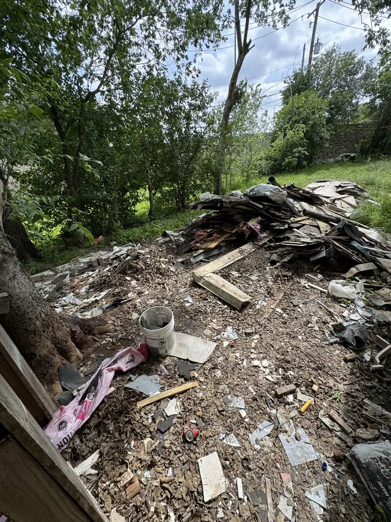 Broken siding, boards and loose debris spread across an Austin yard under a shade tree