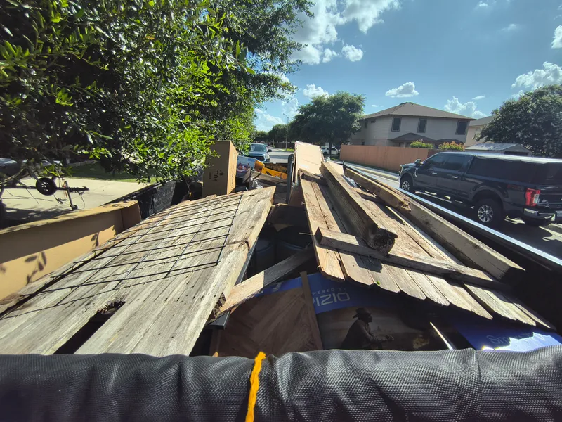 Dump trailer stacked with old deck boards and framing lumber parked at the curb after a deck tear out