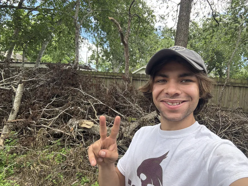 Elite Demo and Junk Removal crew member in front of a large pile of cleared brush and tree limbs at a Martindale property