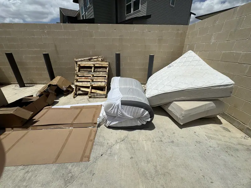 Apartment trash enclosure in New Braunfels with pallets, cardboard, a wrapped mattress and a box spring waiting for pickup