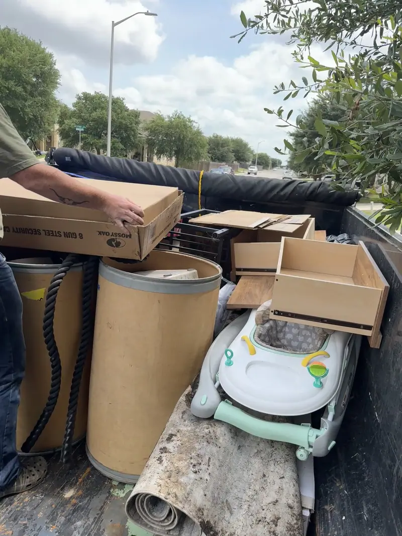 Boxes, cardboard drums and a child's ride on toy being loaded into the dump trailer in New Braunfels
