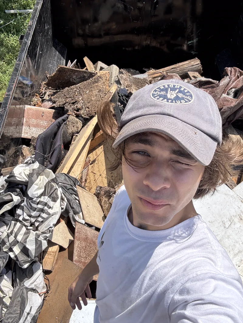 Elite Demo and Junk Removal crew member beside a dump trailer loaded with torn out lumber and demolition debris in San Marcos