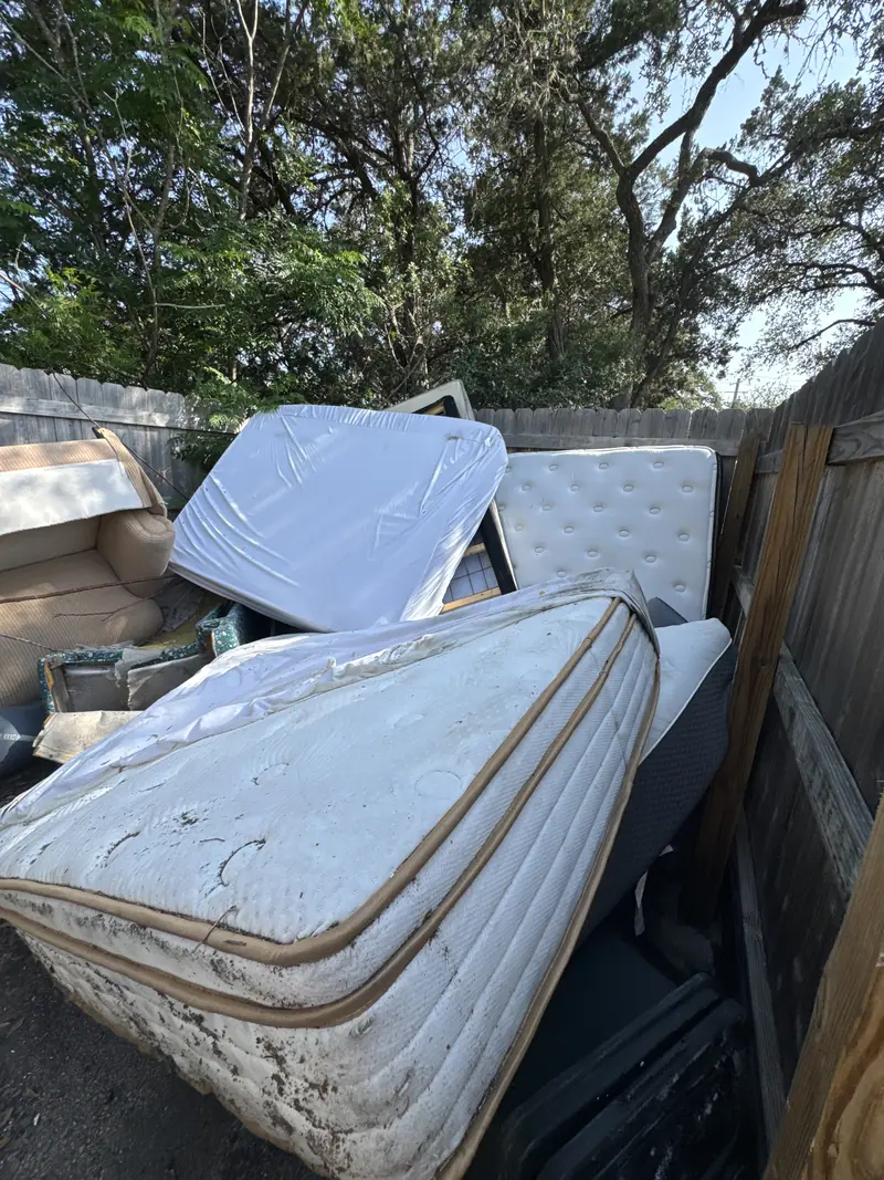 Several used mattresses and box springs stacked against a wooden fence in San Marcos before pickup