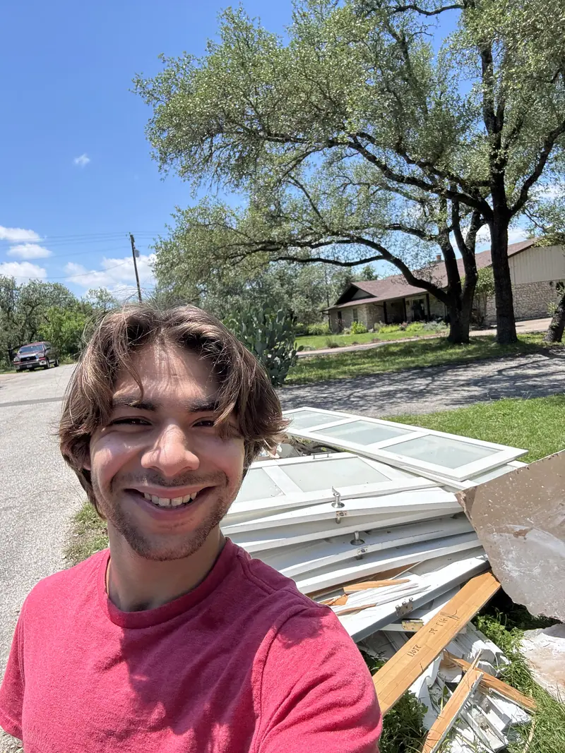 Elite Demo and Junk Removal crew member at the curb beside a pile of old white doors and lumber in southwest Travis County